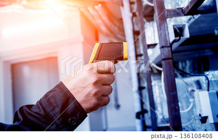 Technician use infrared thermal imaging camera to check temperature at fuse-box 136108408