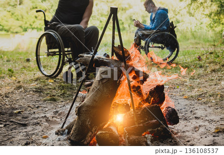 Disabled man resting in a campsite with friends. Wheelchair in the forest Disabled man resting in a campsite with friends. Wheelchair in the forest 136108537