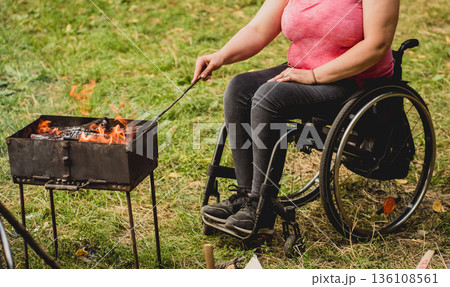 Disabled woman fries meat at the stake in a campsite with friends.  136108561