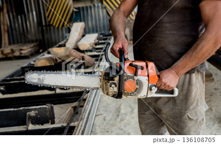 Woodcutter cutting tree with chainsaw on sawmill. Modern sawmill. Woodcutter cutting tree with chainsaw on sawmill. Modern sawmill. 136108705