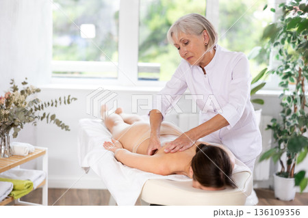 Elderly woman doing back massage to young woman 136109356