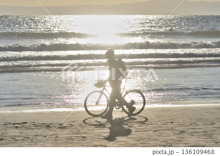 夕方の片瀬西浜海岸の砂浜で自転車を引く男性 夕方の片瀬西浜海岸の砂浜で自転車を引く男性 136109468