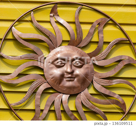 Bronze metal sun decoration on yellow wall of the house. Cooper Sun face with smile. Bronze metal sun decoration on yellow wall of the house. Cooper Sun face with smile. 136109511