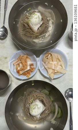 Cold and refreshing Korean naengmyeon noodles, served in a chilled broth with sliced cucumber, radish, and a boiled egg. A savory, tangy dish ideal for hot summer days. 136109681
