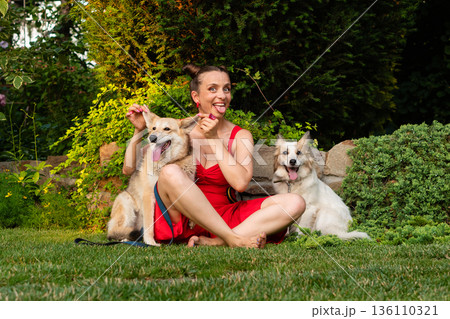Woman sitting with dogs outdoors in garden setting 136110321