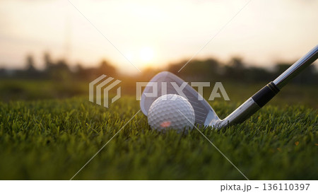 Golf clubs and balls on a green lawn in a beautiful golf course with morning sunshine. Golf clubs and balls on a green lawn in a beautiful golf course with morning sunshine. 136110397