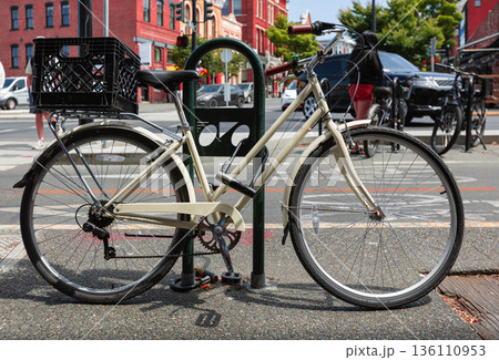 Single bicycle chained up at the bicycle rack on the sidewalk of the street. 136110953