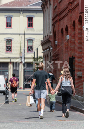 Rear view of a young couple walking down the street holding hands and shopping bags. Rear view of a young couple walking down the street holding hands and shopping bags. 136110954