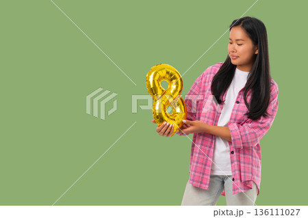 A woman holds a gold number 8 balloon for a special day A woman holds a gold number 8 balloon for a special day 136111027