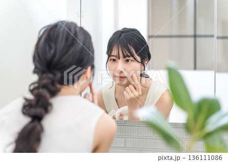 鏡を見ながら顔の肌トラブルをチェックする若いアジア人女性 鏡を見ながら顔の肌トラブルをチェックする若いアジア人女性 136111086