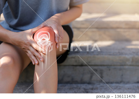 Close-up of hand holding painful injured knee with red inflamed spot and X-ray bone skeleton joint overlay. Medical concept of fracture, arthritis, tendonitis, or muscle ache in outdoor background. Close-up of hand holding painful injured knee with red inflamed spot and X-ray bone skeleton joint overlay. Medical concept of fracture, arthritis, tendonitis, or muscle ache in outdoor background. 136111476