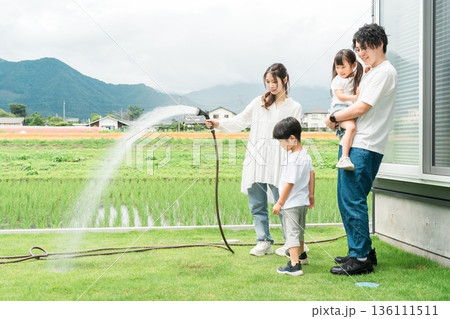 庭の芝生に水やりをする男の子と家族,ファミリー(マイホーム,庭,エクステリア) 庭の芝生に水やりをする男の子と家族,ファミリー(マイホーム,庭,エクステリア) 136111511