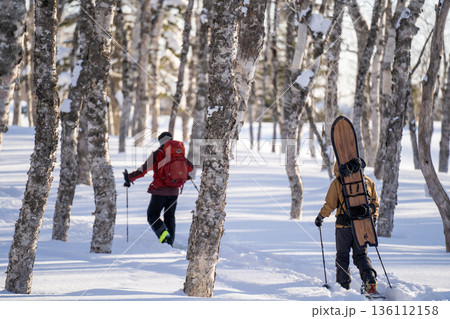 東北海道の雪深い森を進むバックカントリー登山者とスノーボードが描く冬山アウトドアの臨場感ある風景 東北海道の雪深い森を進むバックカントリー登山者とスノーボードが描く冬山アウトドアの臨場感ある風景 136112158