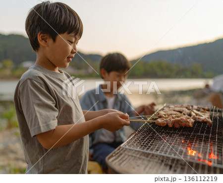 水辺でキャンプ、バーベキュー料理を楽しむ家族 136112219