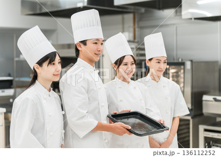 厨房・キッチンに立つコックコート姿の調理師・シェフ・コックの男女 136112252