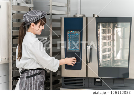 業務用オーブンを取り扱う女性調理スタッフ 業務用オーブンを取り扱う女性調理スタッフ 136113088