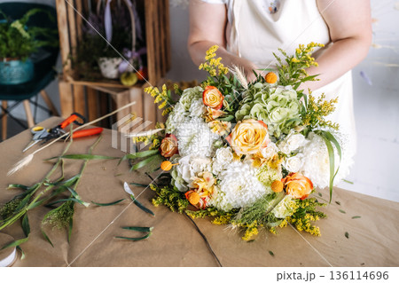 Florist trims botanical stems of large mixed flower bouquet in studio. Creative workspace, commercial flower arrangement, artisan floral business. 136114696