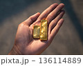 Hand holding real gold bullion bars in warm sunset light. Financial growth, wealth accumulation, and physical gold asset investment. Hand holding real gold bullion bars in warm sunset light. Financial growth, wealth accumulation, and physical gold asset investment. 136114889