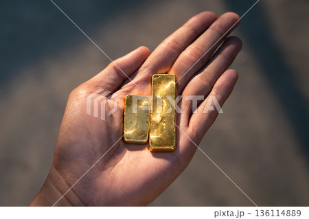 Hand holding real gold bullion bars in warm sunset light. Financial growth, wealth accumulation, and physical gold asset investment. Hand holding real gold bullion bars in warm sunset light. Financial growth, wealth accumulation, and physical gold asset investment. 136114889