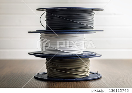 Plastic filament on a spool for 3D printer on wooden table. Plastic filament on a spool for 3D printer on wooden table. 136115746