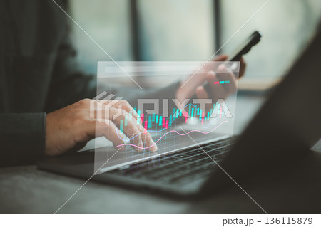 Businessperson analyzing stock market data on laptop with smartphone technology Businessperson analyzing stock market data on laptop with smartphone technology 136115879
