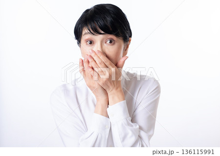 目を見開き両手で口を押え驚いた表情の白いシャツを着たシニア女性 目を見開き両手で口を押え驚いた表情の白いシャツを着たシニア女性 136115991