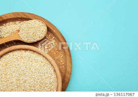 Organic white quinoa seeds in plate and spoon on blue background. 136117067