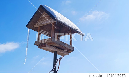 Wooden bird feeder hangs from a branch in a winter park. It's a snowy winter day. Helping the birds Wooden bird feeder hangs from a branch in a winter park. It's a snowy winter day. Helping the birds 136117073