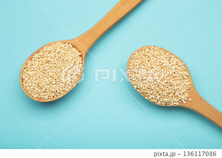 Pile of raw quinoa seeds in wooden spoon on blue background, top view. Pile of raw quinoa seeds in wooden spoon on blue background, top view. 136117086