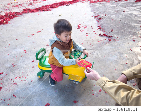 Child On A Toy Ride Receiving Red Envelope for Lunar New Year While Playing 136119311