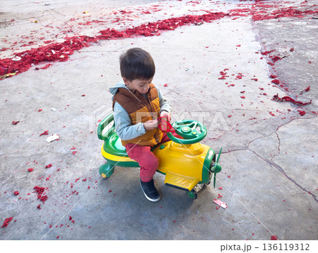 Young Boy Holding a Red Envelope On A Colorful Toy Vehicle 136119312