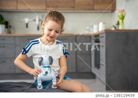 Child playing and interacting with robotic dog on sofa at home. Human robot interaction and digital companionship in modern childhood. Child playing and interacting with robotic dog on sofa at home. Human robot interaction and digital companionship in modern childhood. 136119439