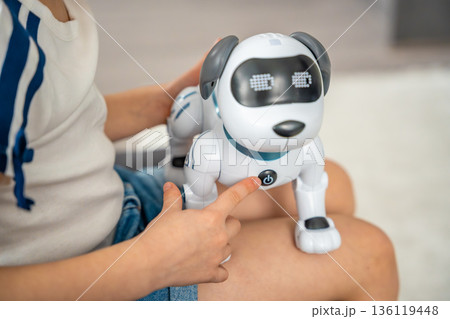 Close up of child hand pressing power button on robotic dog at home. Activation of artificial intelligence device and interaction with smart technology. Close up of child hand pressing power button on robotic dog at home. Activation of artificial intelligence device and interaction with smart technology. 136119448