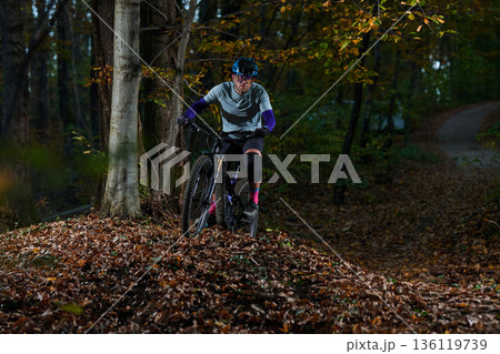 Mountain Biker Navigates Forest Trail in Autumn Leaves With Helmet and Protective Gear Mountain Biker Navigates Forest Trail in Autumn Leaves With Helmet and Protective Gear 136119739