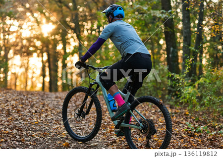 Mountain Biker Riding Through Autumn Forest Trail at Sunset with Sunlit Leaves Mountain Biker Riding Through Autumn Forest Trail at Sunset with Sunlit Leaves 136119812