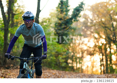 Autumn Forest Trail: Mountain Biker In Sunlight Wearing Helmet And Protective Gear On a Leafy Path 136119815