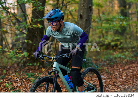 Mountain Biker Races Through Autumn Forest Trail Wearing Helmet and Knee Pads During Outdoor Adventure Mountain Biker Races Through Autumn Forest Trail Wearing Helmet and Knee Pads During Outdoor Adventure 136119834