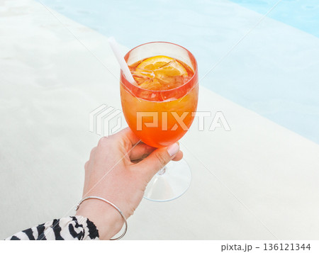 Female hand holds a refreshing orange cocktail Female hand holds a refreshing orange cocktail 136121344