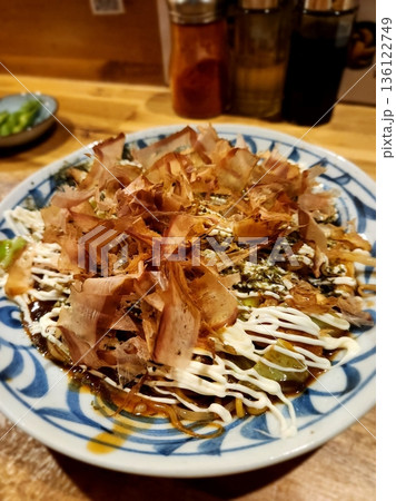 Okonomiyaki, a savory Japanese pancake made with cabbage, flour, and eggs, topped with a flavorful mix of mayo, okonomiyaki sauce, seaweed flakes, and bonito for a rich taste. Okonomiyaki, a savory Japanese pancake made with cabbage, flour, and eggs, topped with a flavorful mix of mayo, okonomiyaki sauce, seaweed flakes, and bonito for a rich taste. 136122749