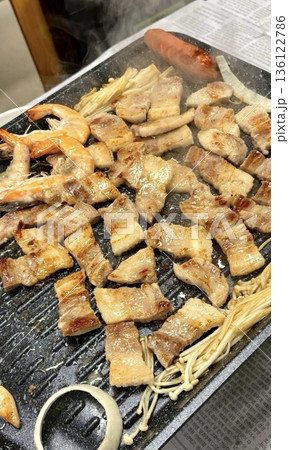 Grilled samgyeopsal, showcasing thick slices of pork belly sizzling on the grill. A popular Korean barbecue dish, capturing the essence of a delicious dining experience. 136122786