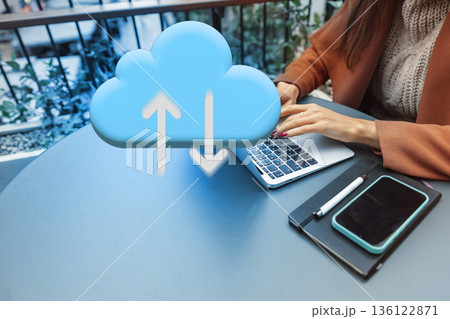 Person working on a laptop at a table with a cloud symbol indicating file upload and download Person working on a laptop at a table with a cloud symbol indicating file upload and download 136122871