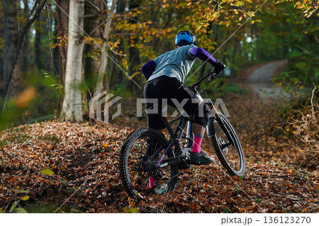 Mountain Biker in Autumn Forest Navigating Leaf-Covered Trail on a Rugged Path During Colorful Fall Sunlight Mountain Biker in Autumn Forest Navigating Leaf-Covered Trail on a Rugged Path During Colorful Fall Sunlight 136123270