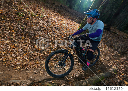 Mountain Biker Rides Through Leaf-Litter Trail in Autumn Forest With Gear, Helmet, and Knee Pads 136123294
