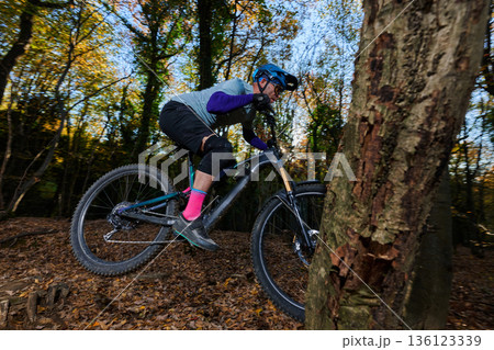 Action-Packed Mountain Biker Navigates Autumn Forest Trail With Speed And Focus Through Leaves And Tree Canopy Sunlight 136123339