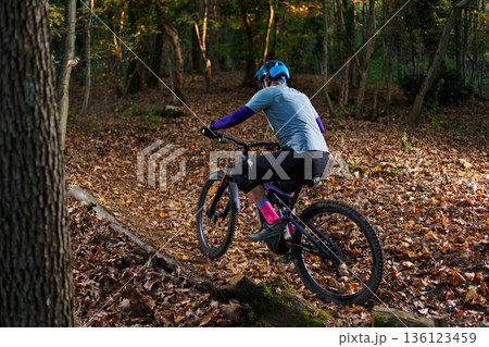 Mountain Biker Navigates Leaf-Covered Trail Through Autumn Forest 136123459