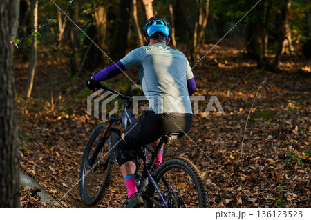 Mountain Biker Riding Through Forest Trail in Autumn Light With Helmet and Gear 136123523