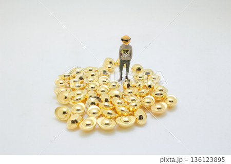 Miniature Figure Standing Calmly On Shiny Gold Ingots 136123895