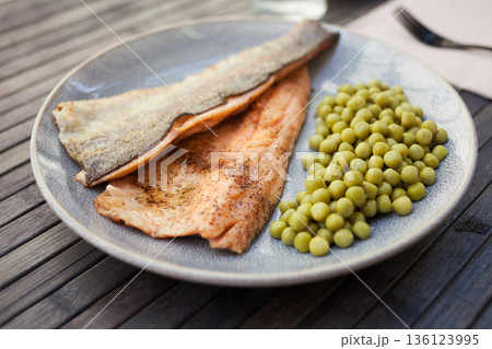 Fried trout fillets served with green peas 136123995