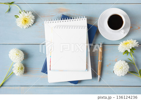 Top view of the desktop. Spiral notebook with an open blank page, pen, white cup with black coffee, dahlia flowers. Festive office desktop concept. Morning coffee cup. Top view of the desktop. Spiral notebook with an open blank page, pen, white cup with black coffee, dahlia flowers. Festive office desktop concept. Morning coffee cup. 136124236
