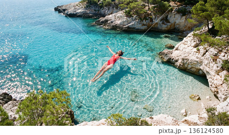 Aerial top view of woman floating in clear blue sea. AI-generated item 136124580